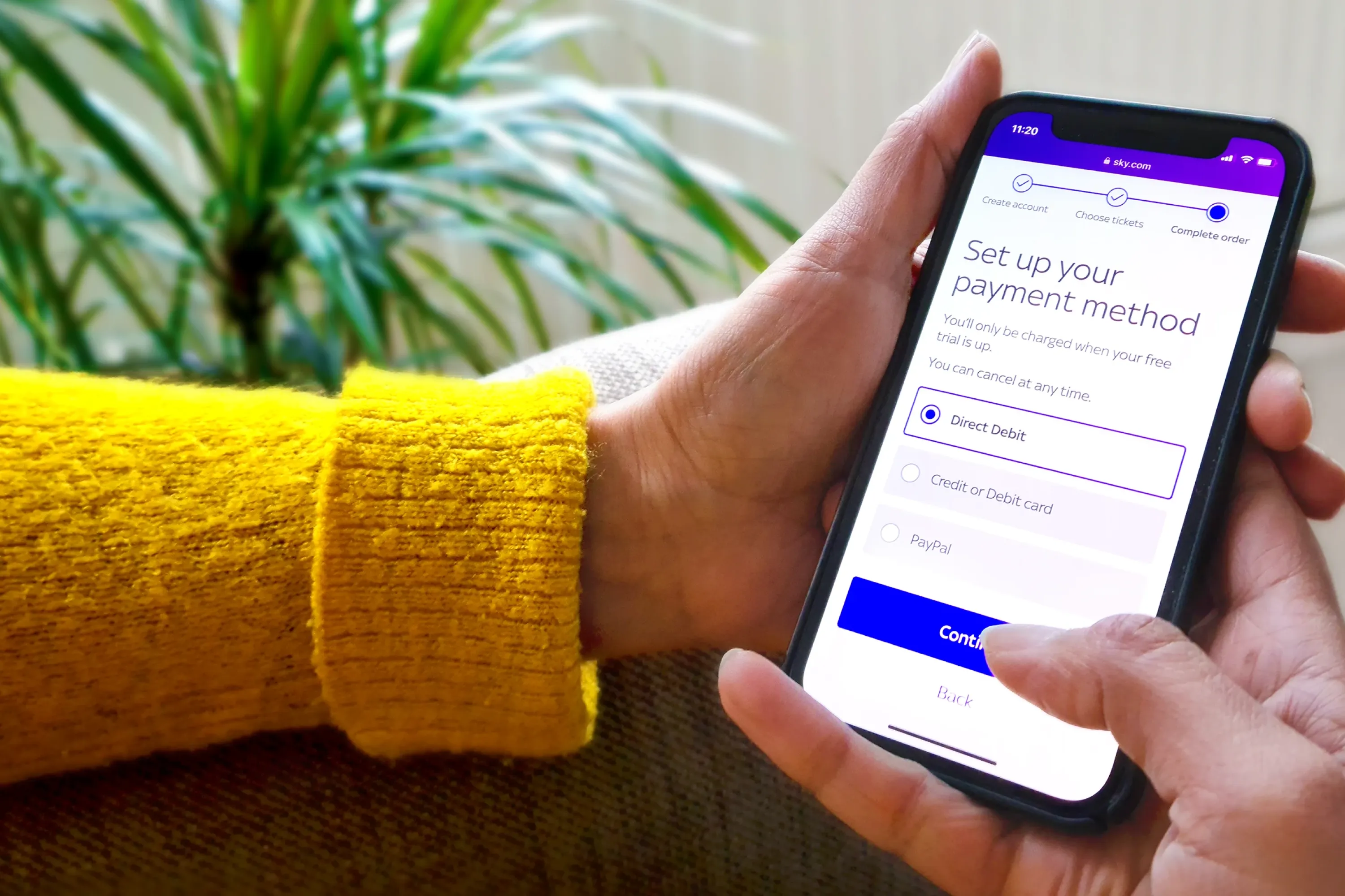 Person holding a smartphone displaying the Sky payment method setup screen, selecting Direct Debit.