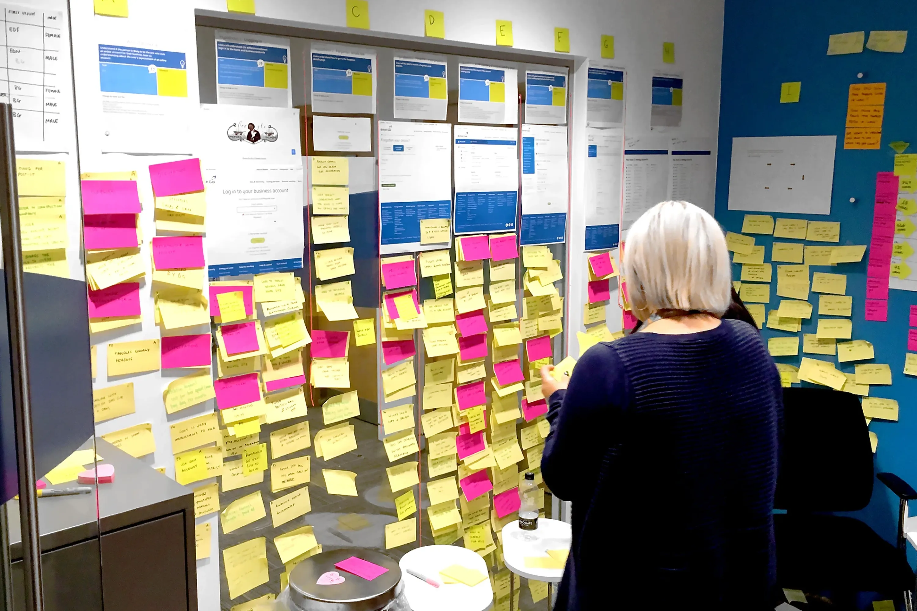 Woman standing in front of a wall covered with website mockups and numerous yellow and pink sticky notes during a design workshop.